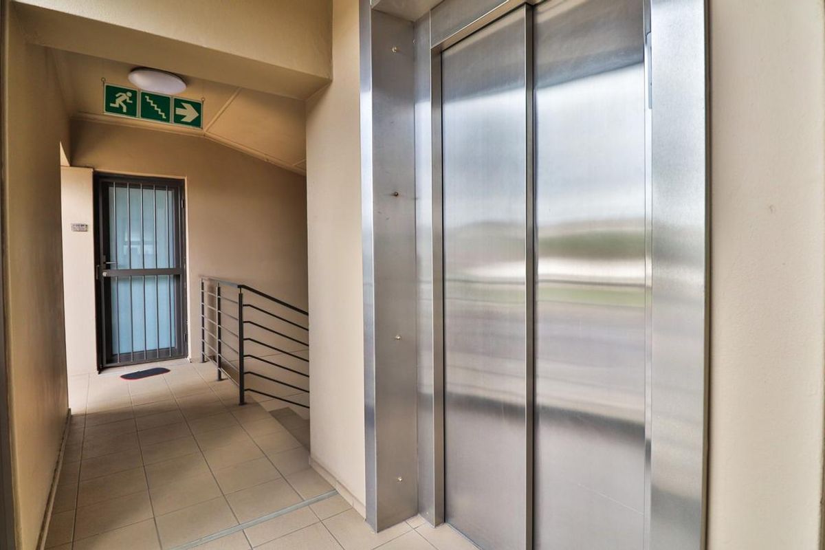 A clean, well-maintained apartment building hallway featuring a stainless steel elevator, tiled flooring, and secure access points.