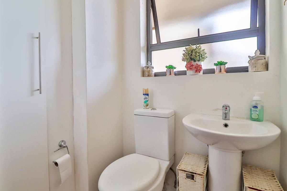 A compact bathroom featuring a white pedestal basin, a standard toilet, and a top-hung window providing natural light.