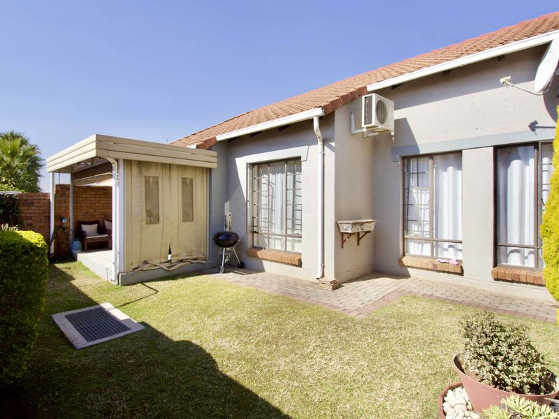 Rear view of the property featuring a small garden, paved area, and a covered patio with a tiled roof and security bars on windows.