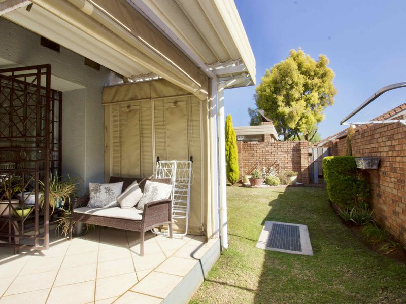 Covered patio area with tiled flooring and retractable awning, leading out to a private, enclosed garden with brick boundary walls.