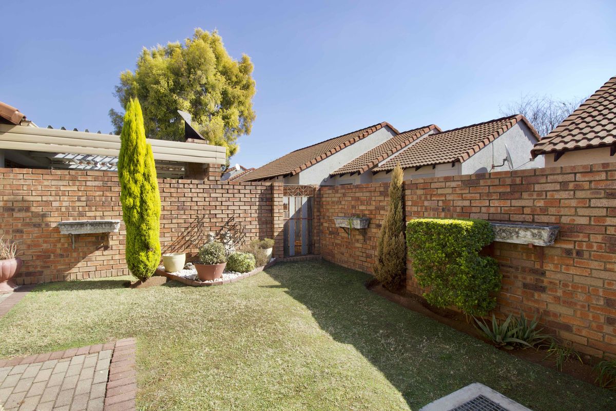 A private rear garden featuring a well-maintained lawn, face brick boundary walls, paved pathways, and integrated concrete planter boxes.