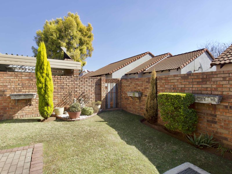 A private rear garden featuring a well-maintained lawn, face brick boundary walls, paved pathways, and integrated concrete planter boxes.