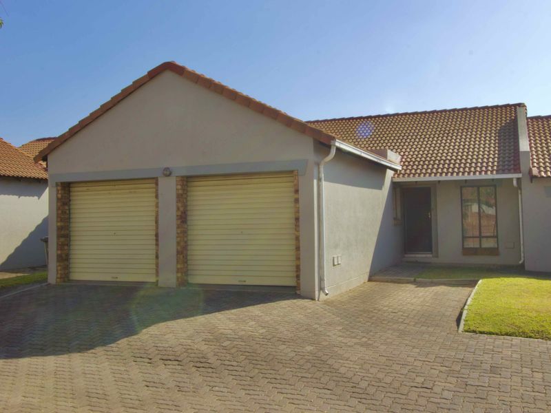 Front exterior view of a cluster home featuring a double garage, paved driveway, and tiled roof.