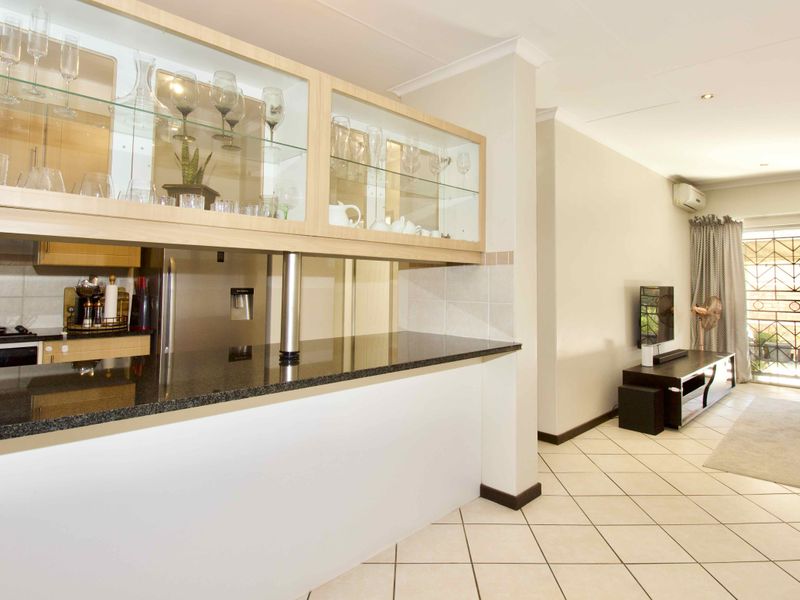 Open-plan living area featuring a kitchen with granite countertops, glass-fronted cabinetry, and tiled flooring, leading to a bright lounge with air conditioning.