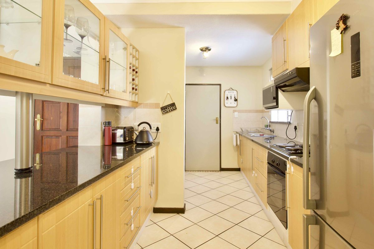 A functional galley-style kitchen featuring light wood cabinetry, dark granite countertops, built-in appliances, and tiled flooring.