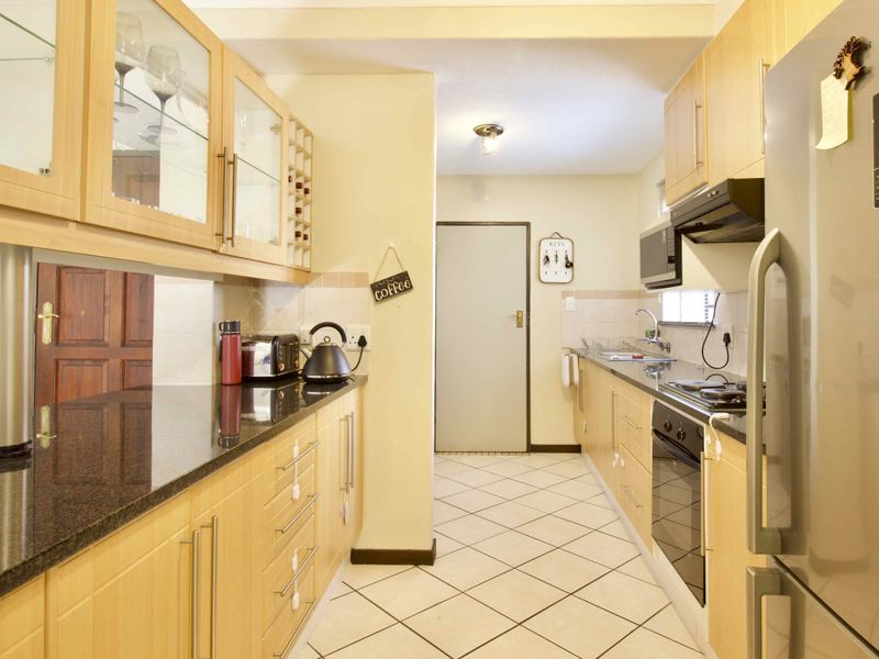 A functional galley-style kitchen featuring light wood cabinetry, dark granite countertops, built-in appliances, and tiled flooring.