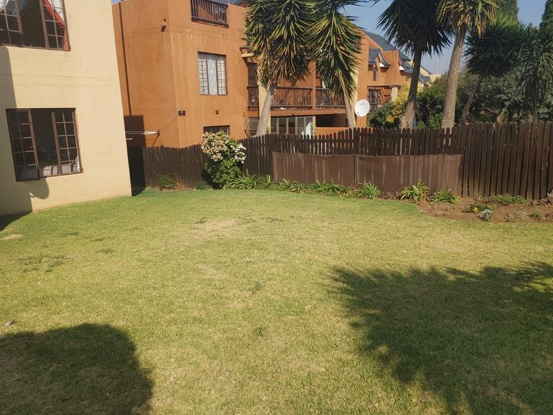 A private rear garden area featuring a lawn and wooden perimeter fencing, adjacent to the townhouse building structure.