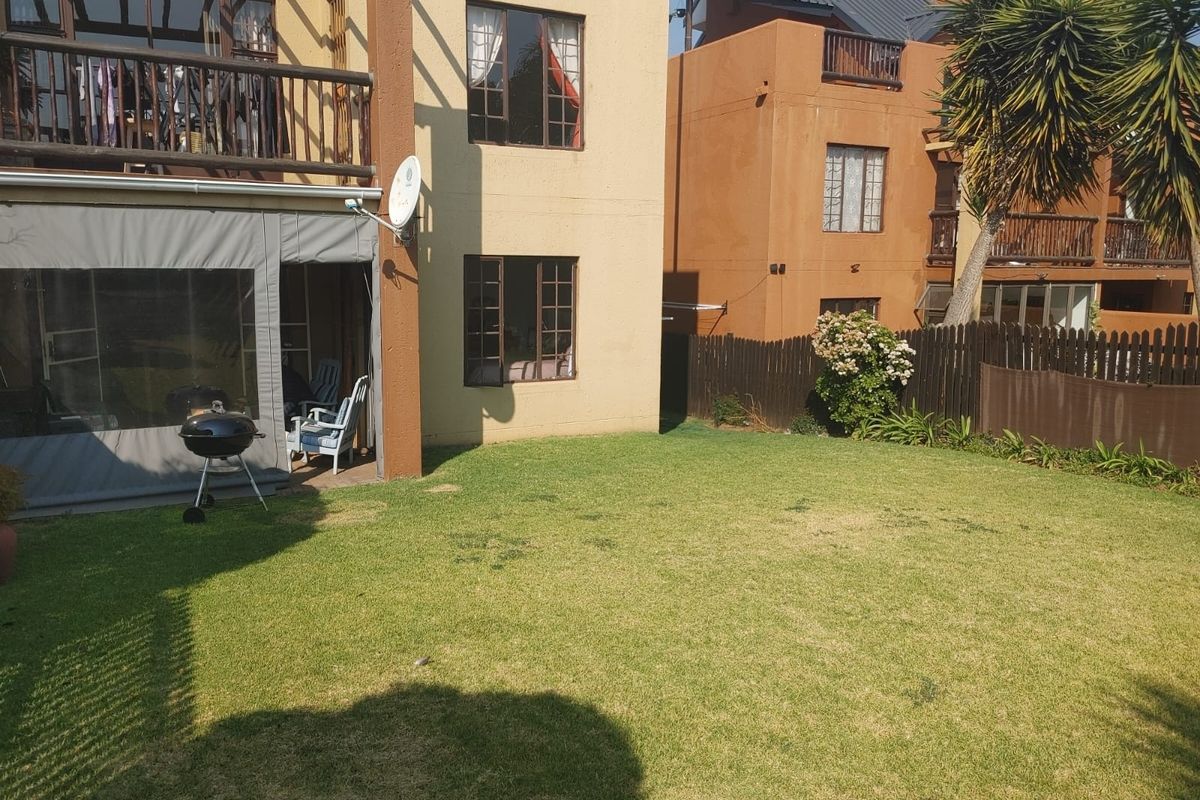 Rear view of the townhouse featuring a private garden, a covered patio area, and an upper-level balcony with wooden railings.