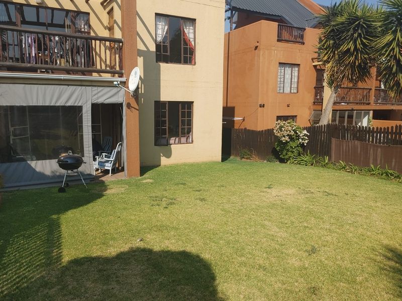 Rear view of the townhouse featuring a private garden, a covered patio area, and an upper-level balcony with wooden railings.