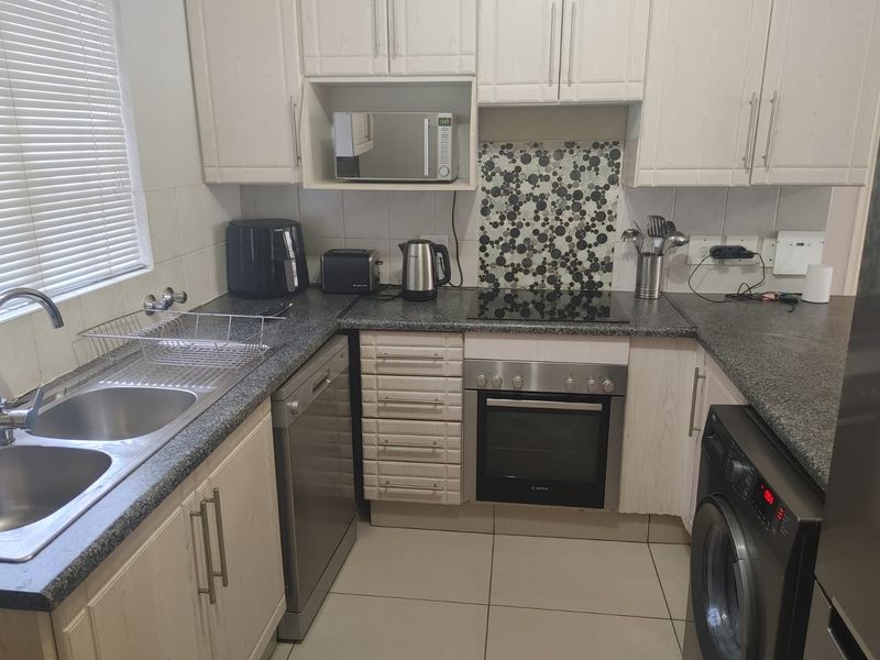 Compact kitchen featuring light wood-grain cabinetry, granite countertops, mosaic splashback, and integrated appliances including an oven and hob.