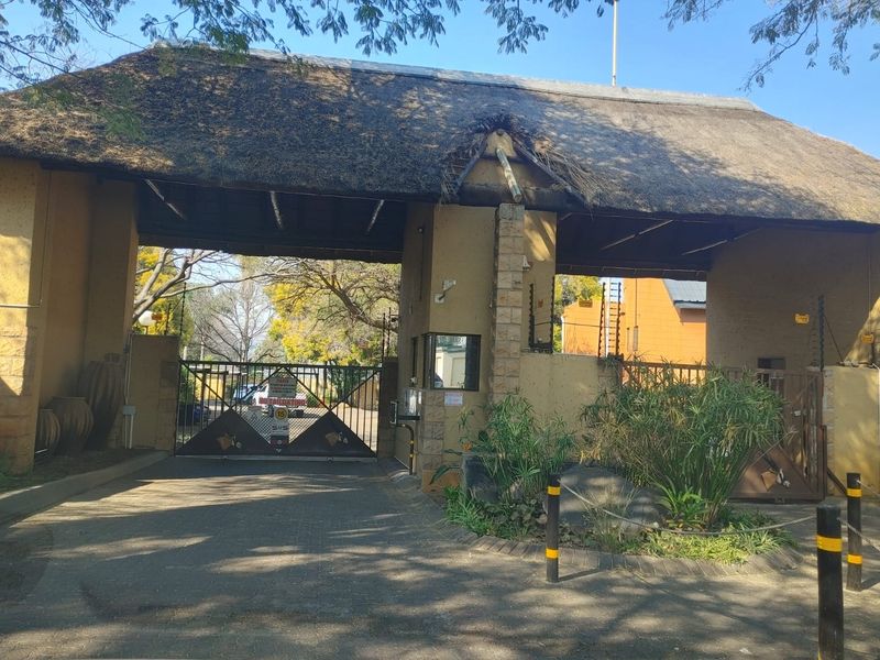 The entrance to the townhouse complex features a gated security access point with a traditional thatched roof structure and perimeter electric fencing.