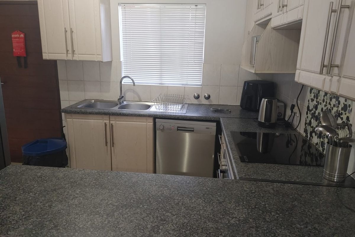 A functional kitchen featuring light-toned cabinetry, granite countertops, a double sink, and a built-in electric hob with a tiled backsplash.