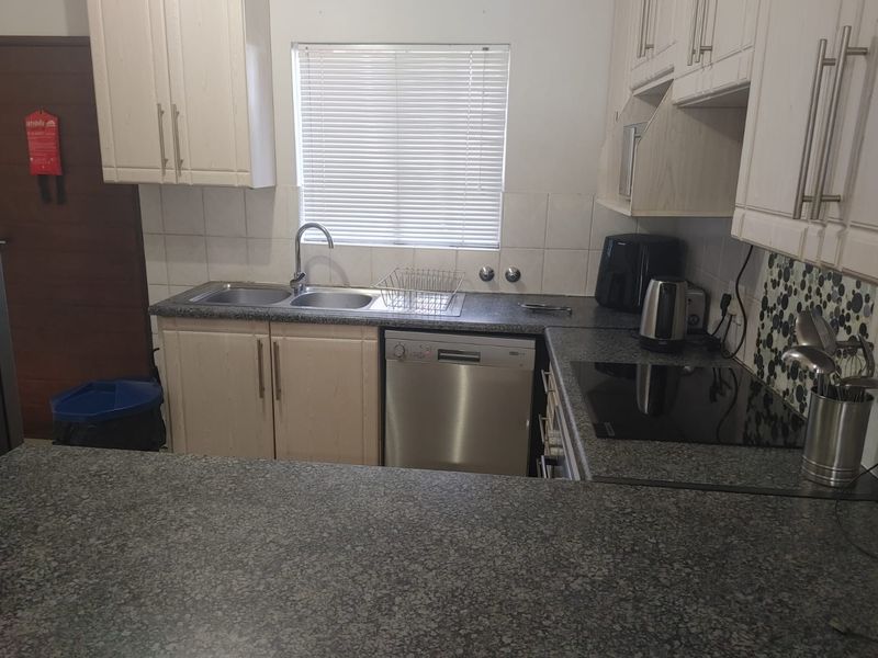 A functional kitchen featuring light-toned cabinetry, granite countertops, a double sink, and a built-in electric hob with a tiled backsplash.