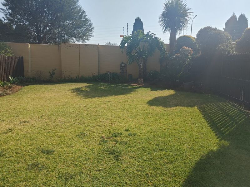 A private rear garden featuring a well-maintained lawn, enclosed by a perimeter wall with electric fencing and timber side fencing.