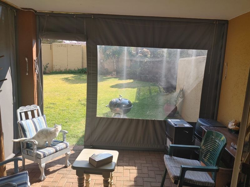 Covered patio area featuring brick paving and a roll-up canvas enclosure, overlooking a private garden with boundary walls.
