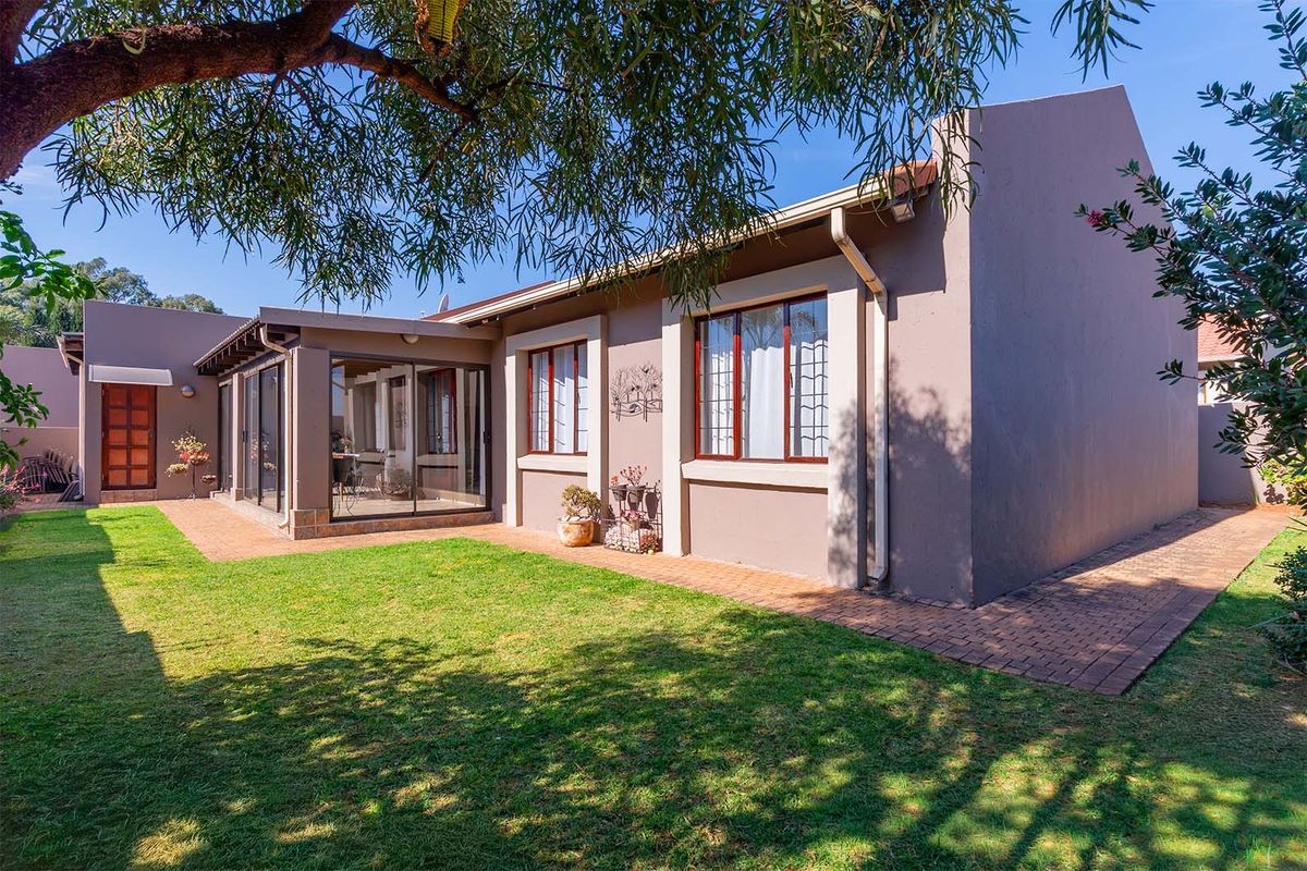 A well-maintained rear exterior view of the cluster home featuring a paved patio area, sliding glass doors, and a neat garden lawn.