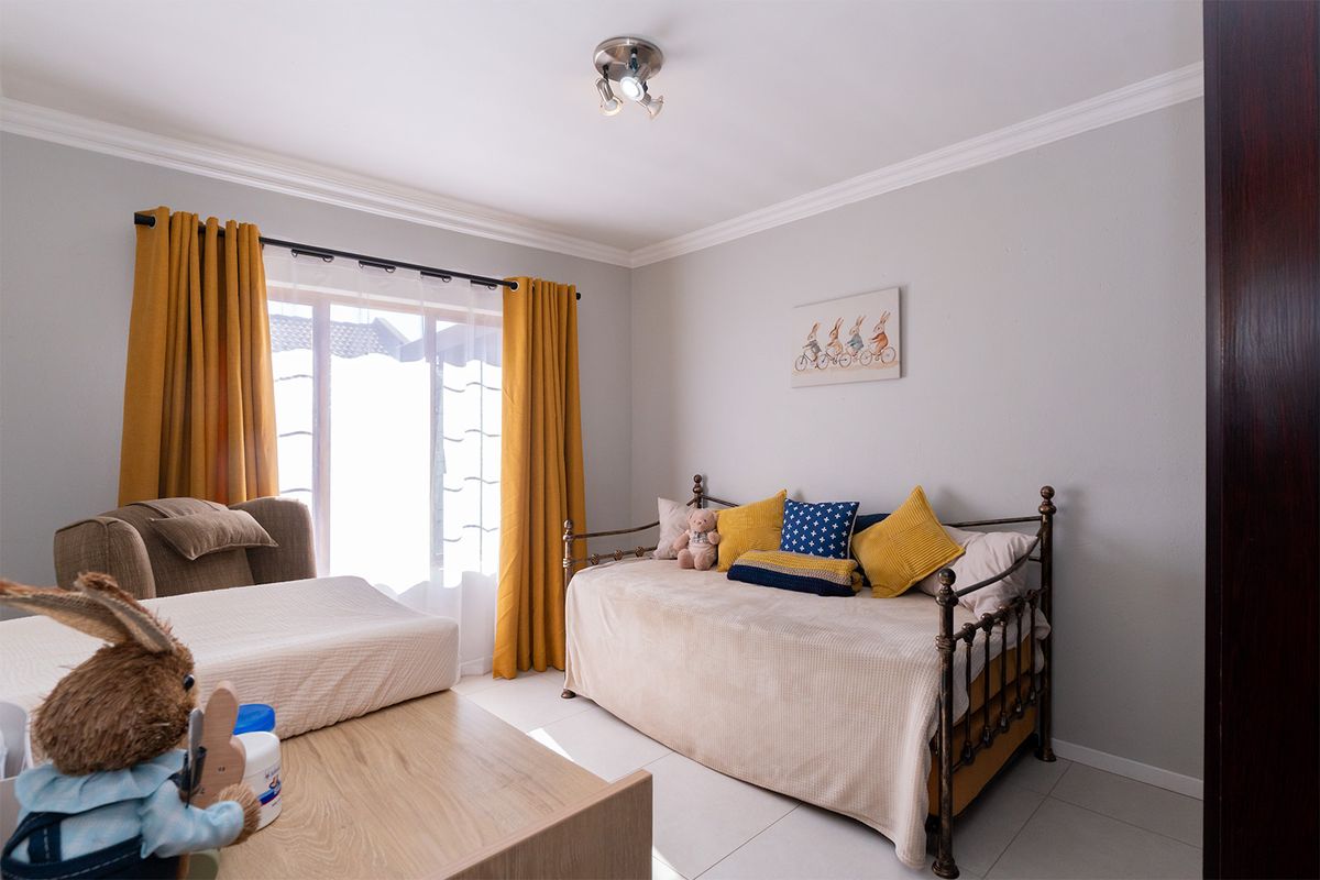 A well-maintained bedroom featuring neutral wall tones, tiled flooring, decorative ceiling cornicing, and a modern ceiling-mounted spotlight fixture.