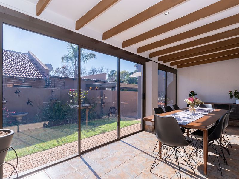 A bright, enclosed patio featuring exposed timber ceiling beams, large sliding glass doors, and tiled flooring, offering a seamless transition to the garden.