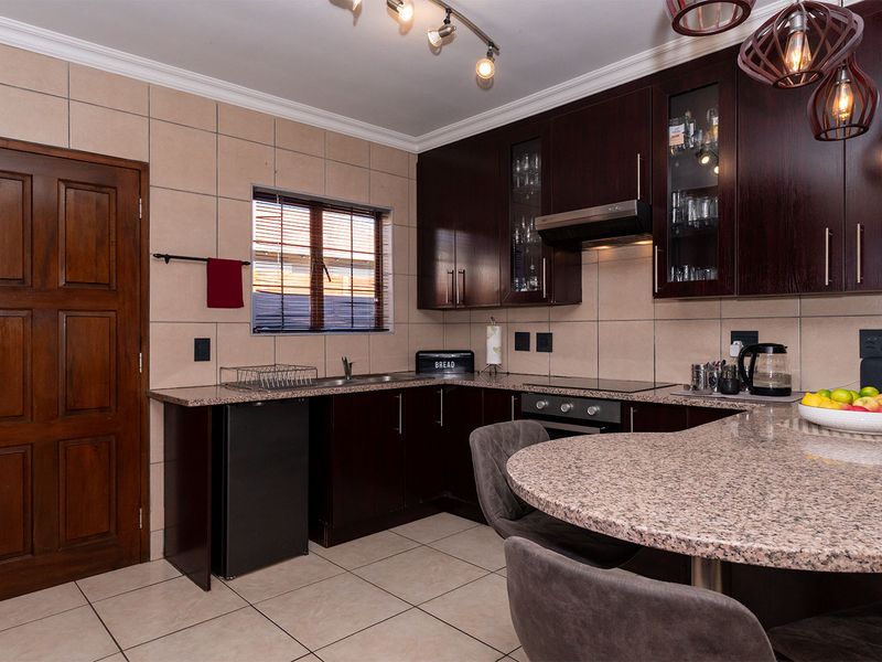 A well-maintained kitchen featuring dark wood cabinetry, granite countertops, a built-in oven, and a breakfast nook, complemented by neutral tiled finishes.