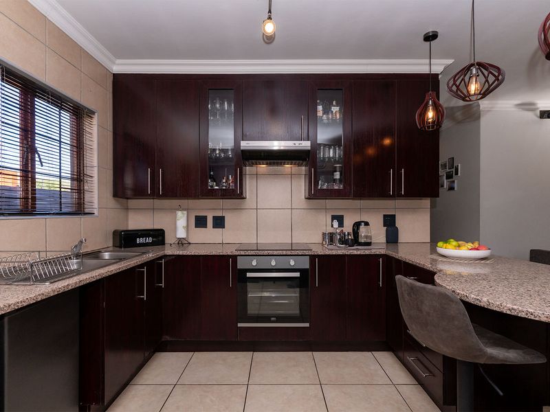 A well-maintained kitchen featuring dark wood cabinetry, granite countertops, built-in oven, electric hob, and a breakfast nook area.