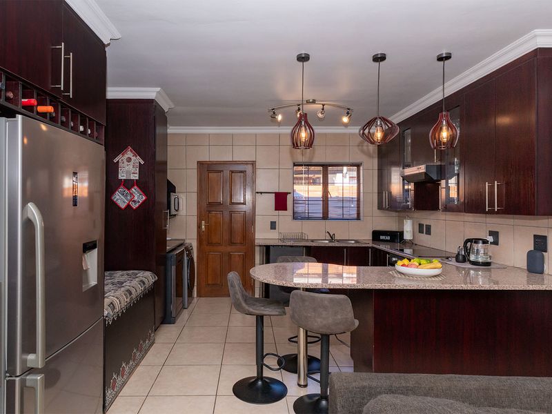 A well-appointed kitchen featuring dark wood cabinetry, granite countertops, a breakfast bar, and modern pendant lighting, complemented by neutral tiled flooring and backsplash.