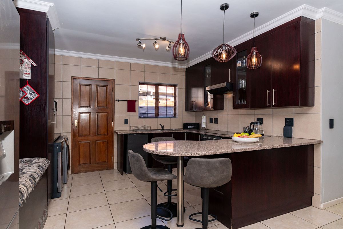 A well-maintained kitchen featuring dark wood cabinetry, granite countertops, a breakfast bar, and tiled flooring, offering a functional and classic cooking space.