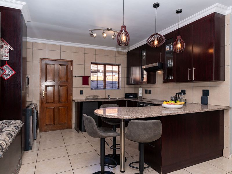 A well-maintained kitchen featuring dark wood cabinetry, granite countertops, a breakfast bar, and tiled flooring, offering a functional and classic cooking space.