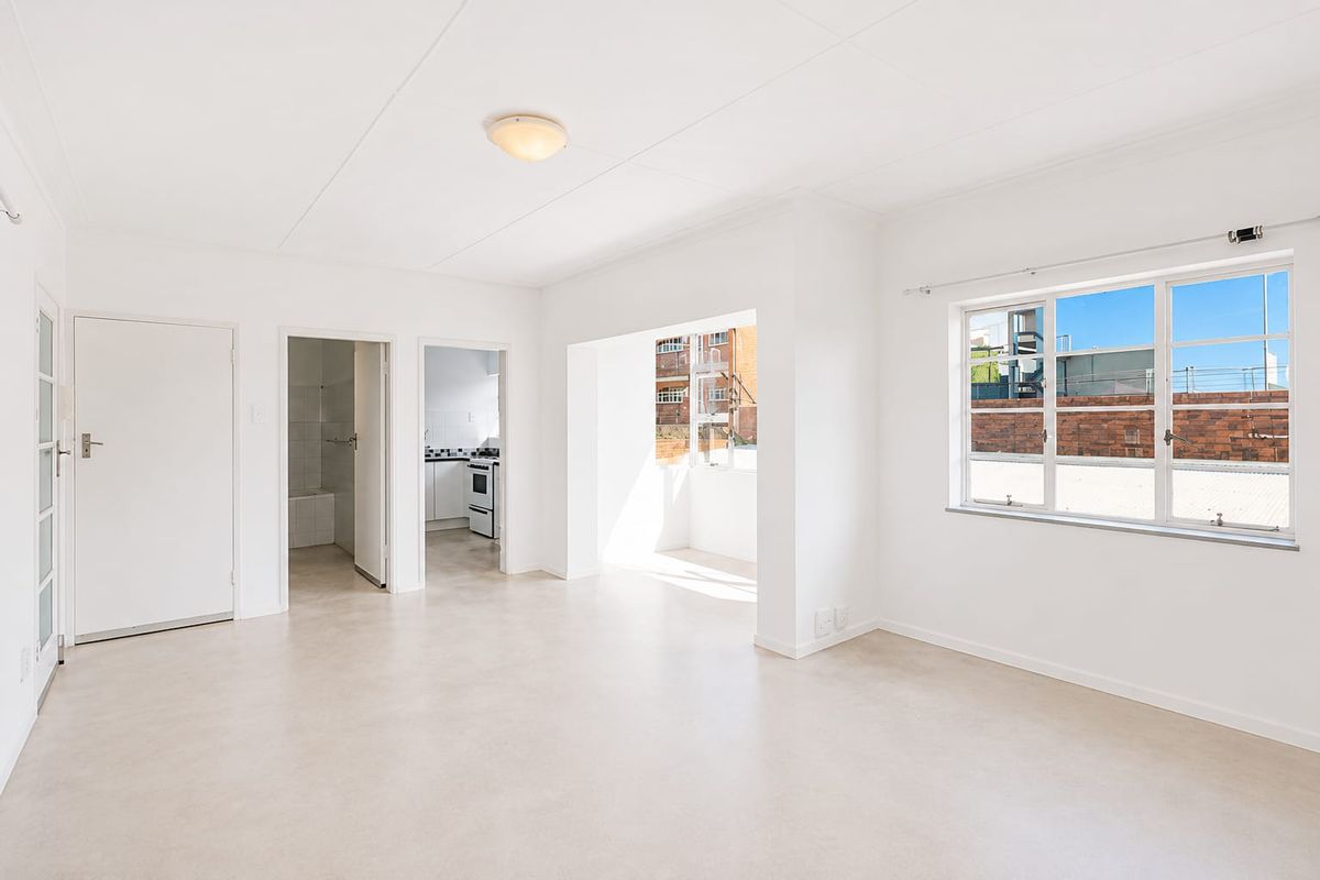 A bright, vacant living area featuring neutral vinyl flooring, clean white walls, and large windows allowing for ample natural light.