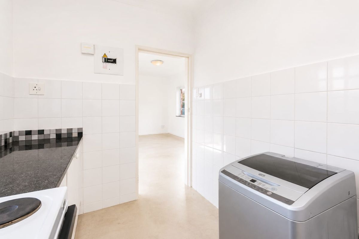 A functional kitchen area featuring tiled splashbacks, granite countertops, and an integrated electric stove, leading into an adjacent living space.