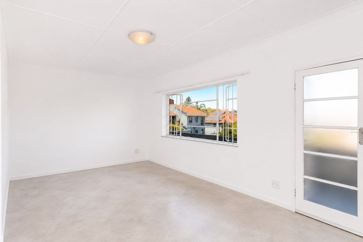 A bright, empty bedroom featuring neutral tiled flooring, a large casement window with security bars, and a frosted glass door.
