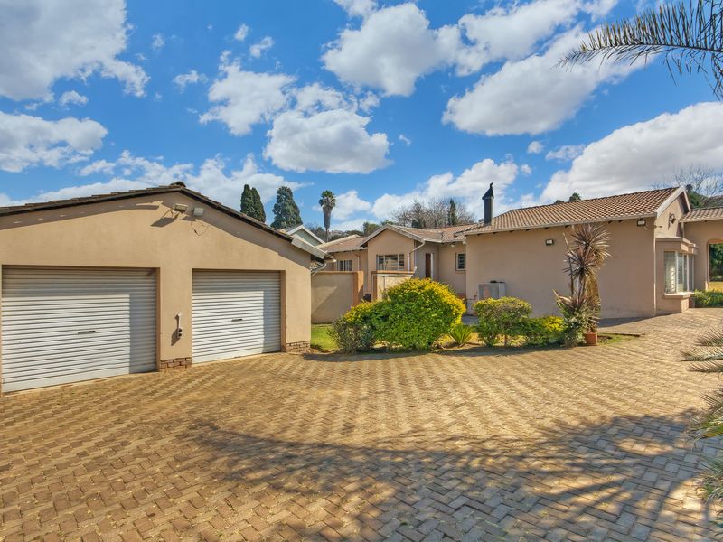 Front view of the property featuring a double garage with roller shutter doors and an extensive paved driveway leading to the main entrance.