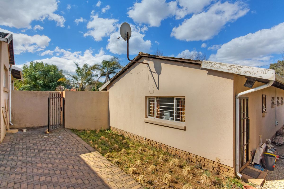 Rear exterior view of the property featuring a paved walkway, security gates, burglar bars, and a satellite dish mounted on the roof.