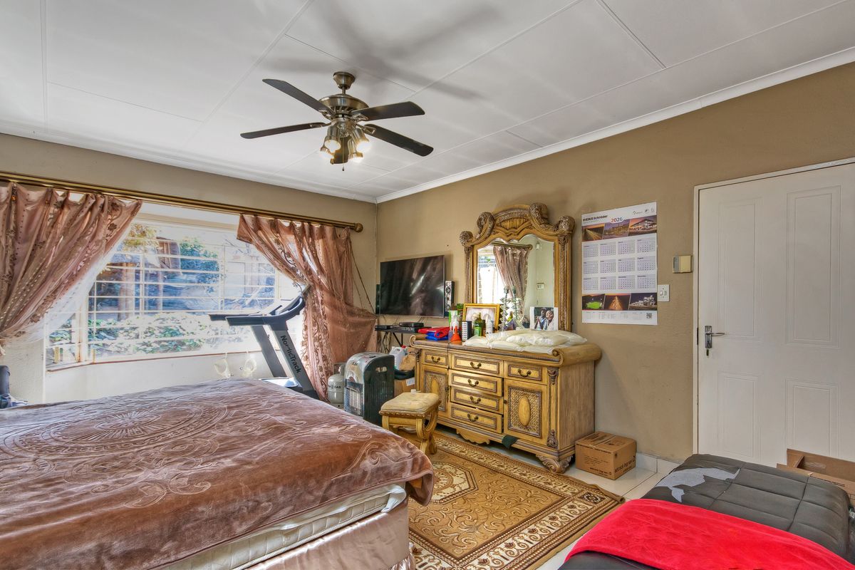 A bedroom featuring tiled flooring, a ceiling fan, and security bars on the window. The room requires cosmetic updates to improve its overall condition.
