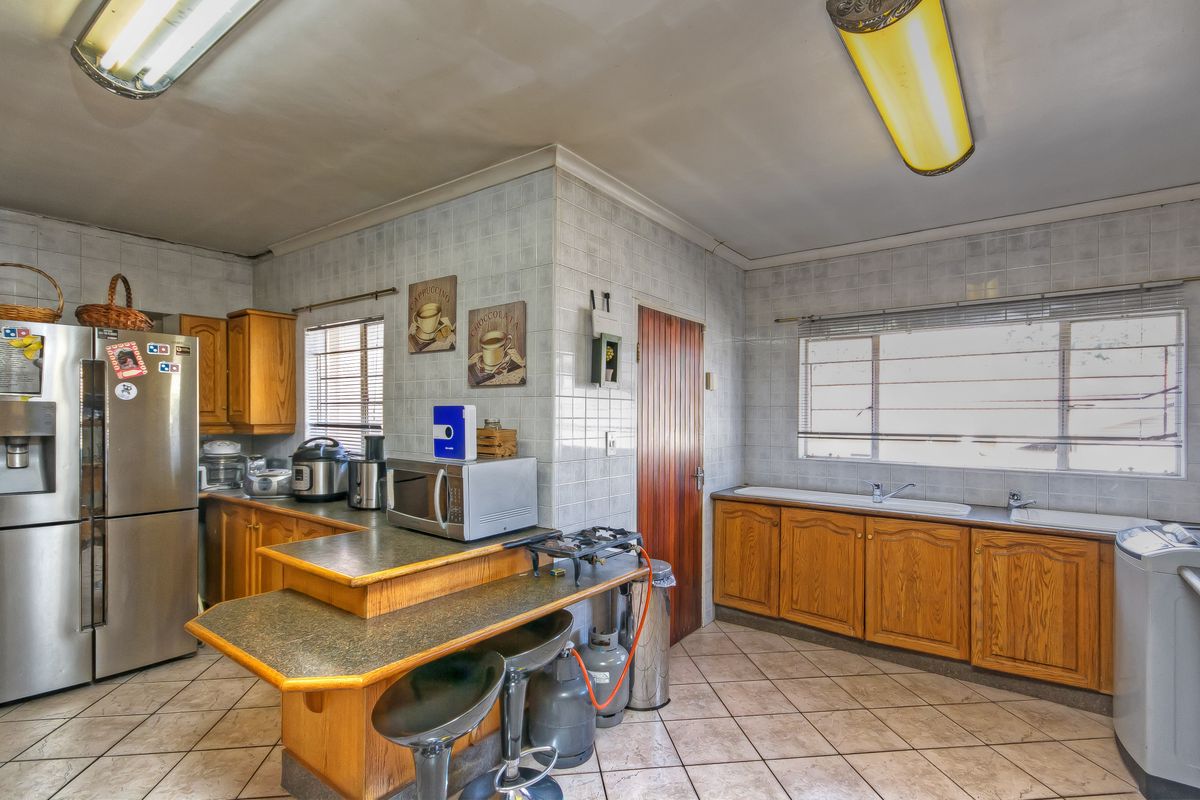 A dated kitchen featuring wooden cabinetry, laminate countertops, tiled walls, and a double basin sink, offering significant potential for modernization and renovation.