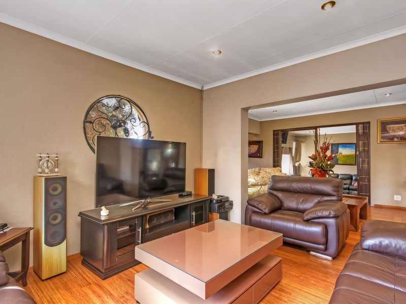 A comfortable living room featuring warm-toned laminate flooring and coved ceilings, with an open-plan flow into the adjacent living space.