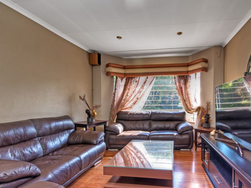 A comfortable living room featuring warm laminate flooring, a large bay window with natural light, and recessed ceiling lighting.