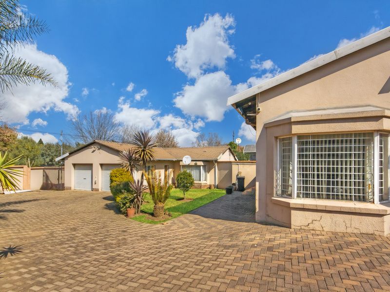 Front view of the property featuring a paved driveway, double garage, and a bay window with security bars.