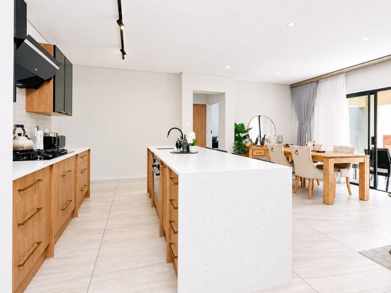 Modern open-plan kitchen and dining area featuring a large quartz island, wood-finish cabinetry, gas hob, and seamless access to the outdoor patio.