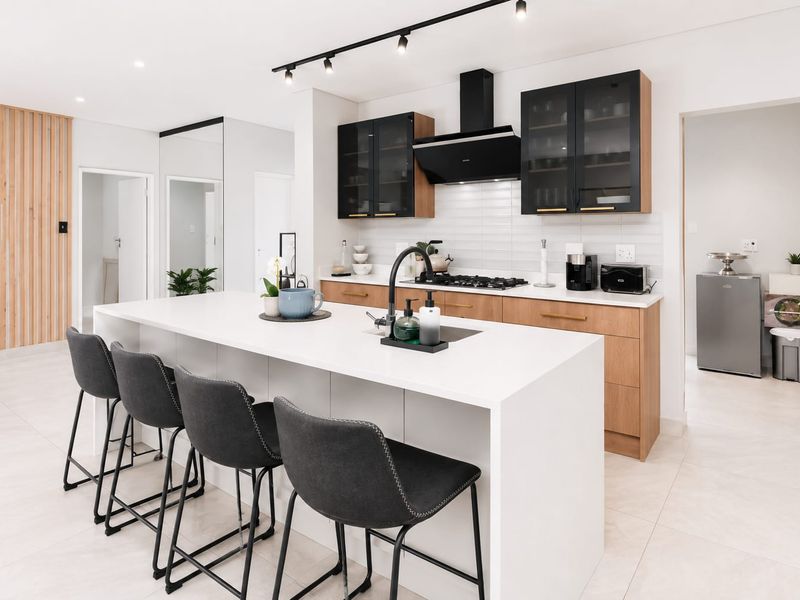Modern open-plan kitchen featuring a large central island, sleek timber and black cabinetry, gas hob, and contemporary track lighting.