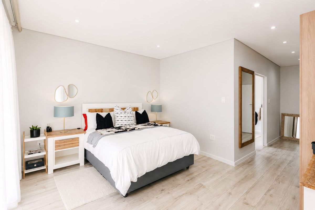 A bright and modern bedroom featuring light-toned laminate flooring, recessed downlighting, and an integrated air conditioning unit.