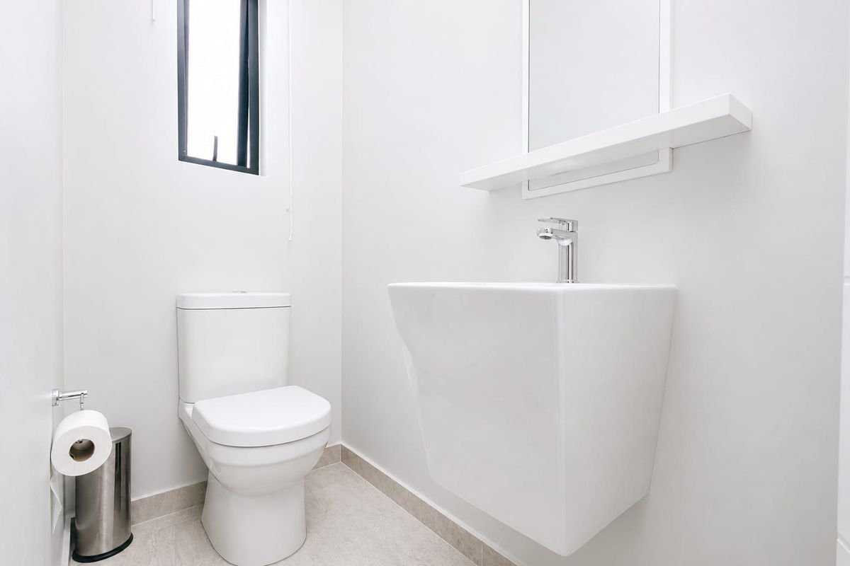 A clean, modern guest bathroom featuring a wall-mounted basin, chrome fixtures, and a minimalist aesthetic with neutral tiled flooring.