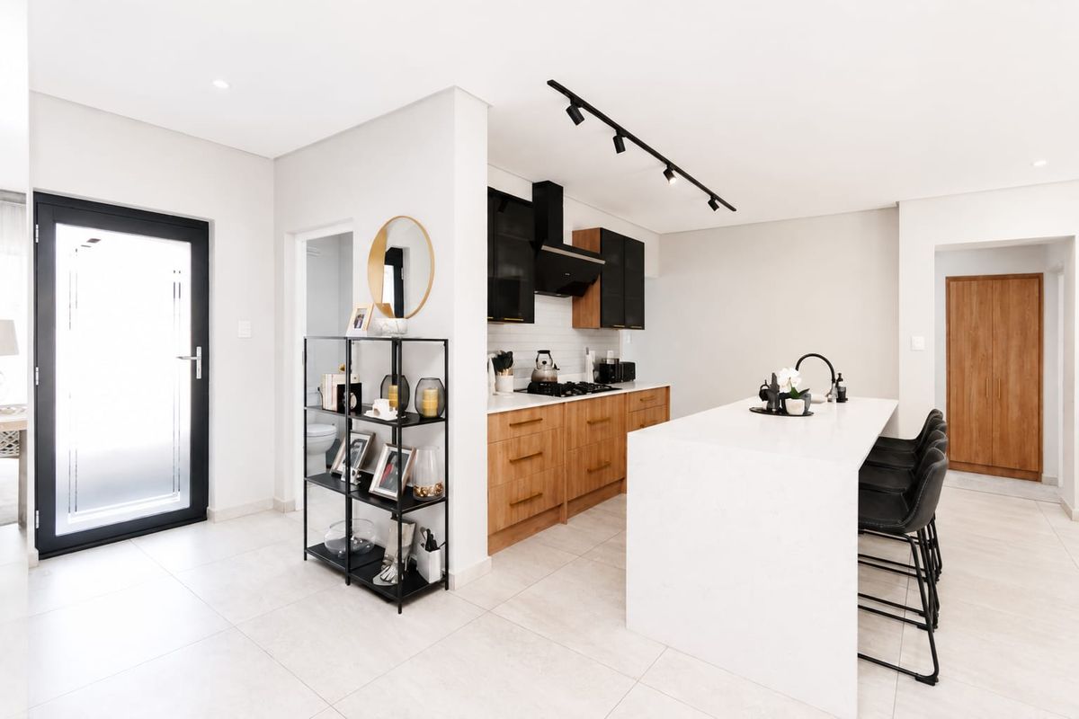 Modern open-plan kitchen featuring a large central island with quartz countertops, sleek wood and black cabinetry, gas hob, and contemporary track lighting.
