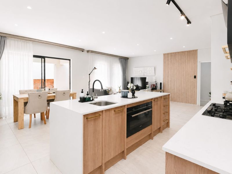Modern open-plan living area featuring a contemporary kitchen with a central island, timber cabinetry, integrated appliances, and seamless flow to the dining space.