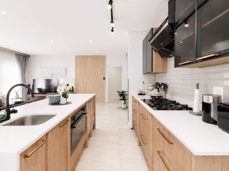 Modern open-plan kitchen featuring timber cabinetry, white stone countertops, a central island with sink, and integrated gas cooktop with extractor fan.
