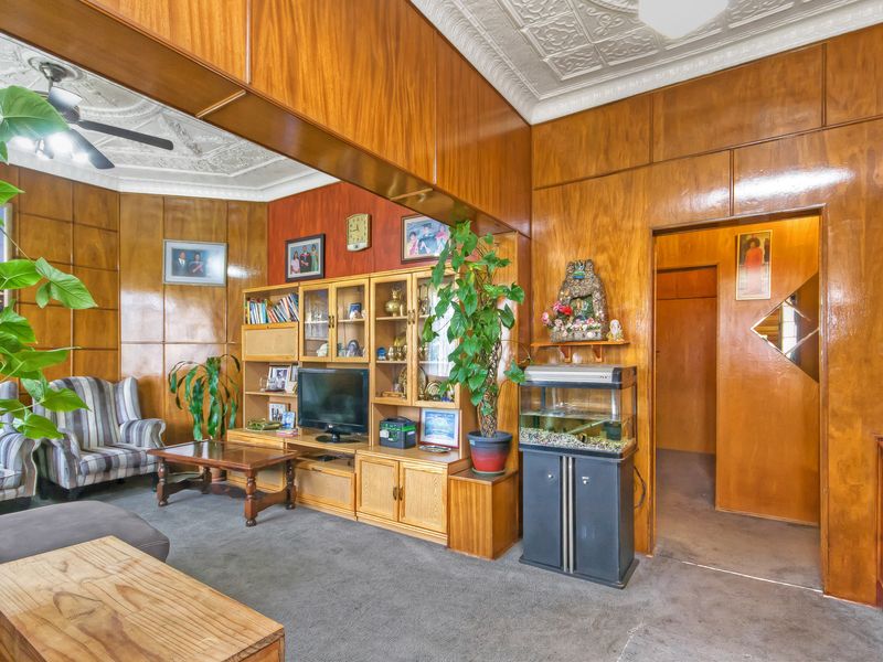A living room featuring extensive wood paneling, an ornate pressed metal ceiling, and a ceiling fan, offering a classic, dated aesthetic.