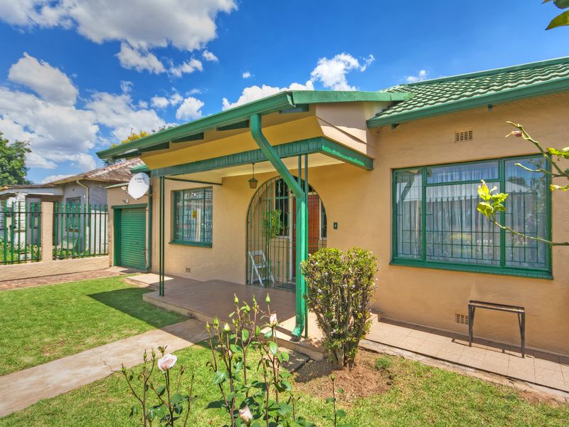 Front elevation of a single-story house featuring a covered porch, tiled roof, metal security gate, and a well-maintained front garden with paved walkway.