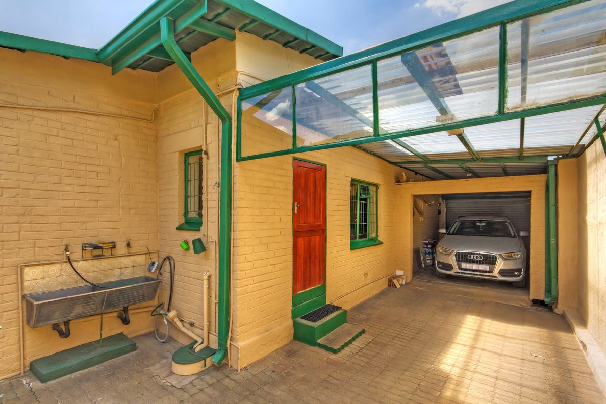 Rear exterior area featuring a paved carport, metal utility sink with tiled splashback, and direct access to a garage.