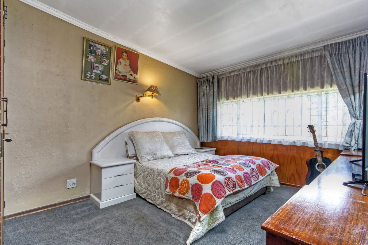 A bedroom featuring wood paneling, a built-in headboard, wall-mounted lighting, and security bars on the window, offering a dated aesthetic ready for modernization.
