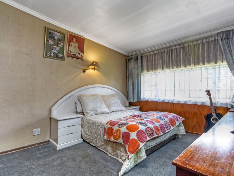 A bedroom featuring wood paneling, a built-in headboard, wall-mounted lighting, and security bars on the window, offering a dated aesthetic ready for modernization.