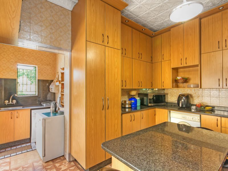 Open plan kitchen featuring extensive wooden cabinetry, granite countertops, and decorative ceiling tiles, with an adjoining scullery area.
